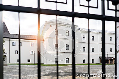 Big white Building and low sun shining seen through the gate. View through fence Stock Photo