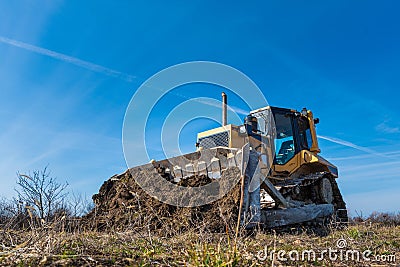 A big yellow bulldozer pushes the ground and makes a new road Stock Photo