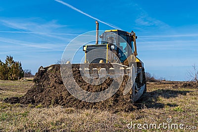 A big yellow bulldozer pushes the ground and makes a new road Stock Photo