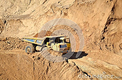 Big yellow dump truck transporting sand in an open-pit mining quarry. Mining quarry for the production of crushed stone, sand and Editorial Stock Photo