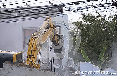 Big yellow excavator removal home building by destroy concrete wall. uproot old construction house for development new project Stock Photo