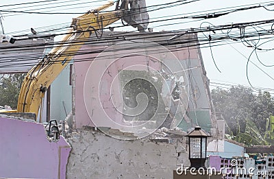 Big yellow excavator removal home building by destroy pik concrete wall. uproot old construction house for development new project Stock Photo