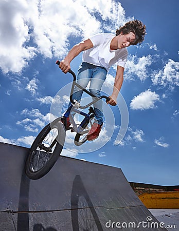 Bike, jump and teen on ramp for sport performance, ride or training for event at park with sky. Bicycle, stunt or kid Stock Photo