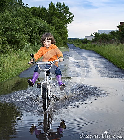 Bike in the park moving through puddle on rainy day. Boy on a bicycle at asphalt road in summer Stock Photo