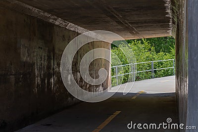 Bike path tunnel under roadway, sharp curve and railing beyond Stock Photo
