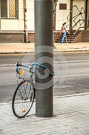 Bike tied to a post. In the background a walking woman Editorial Stock Photo