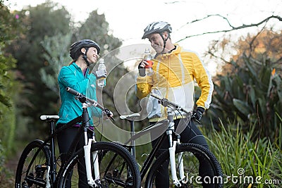 Biker couple standing with bicycle drinking water in forest Editorial Stock Photo