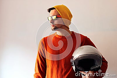 Biker dressed in orange and with a yellow cap and sunglasses with his gray helmet in his hand Stock Photo