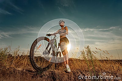 Biker-girl at the sunset with mountain bike. Woman with bicycle at sunrise on trail. Stock Photo