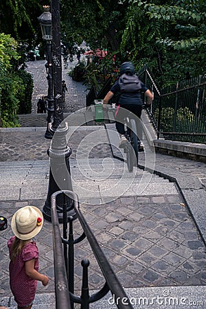 Biker going down stairs with his bike while a young girl looking at him in Montmartre, Paris, France Editorial Stock Photo