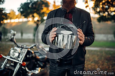 Biker holds helmet in hands, chopper on background Stock Photo