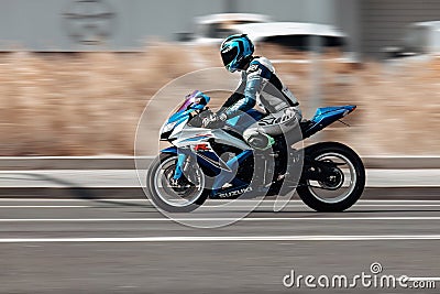Biker ride Suzuki motorcycle on the city road with motion blurred background. Motorcyclist in cyan helmet and jacket on blue Editorial Stock Photo