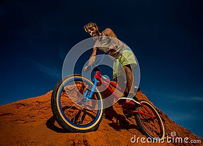 Biker rides on the high mountains of red sand dunes . Stock Photo