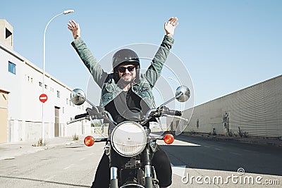 Happy bearded biker staying with unknown big chopper bike on road with hands up. Stock Photo