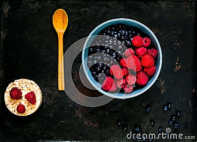 Bilberry and raspberries in blue bowl, the concept of organic berries bowl on vintage rusty metal background. Stock Photo