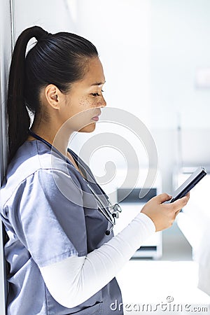 Biracial female doctor wearing scrubs using smartphon in hospital Stock Photo