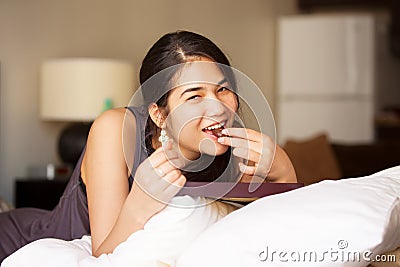 Biracial teen girl lying on bed eating chocolates, smiling Stock Photo