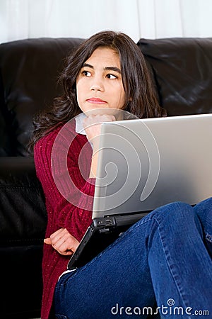 Biracial teen girl sitting against couch with laptop Stock Photo