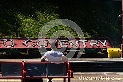 BIRMINGHAM, UK - March 2018 One Man Sitting in the Steel Bench at the Coventry Train Station. Big Welcome Greeting Sign Editorial Stock Photo