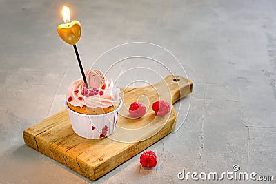 Birthday cupcake with a candle in the form of a heart on a wooden board with raspberries on a gray background Stock Photo