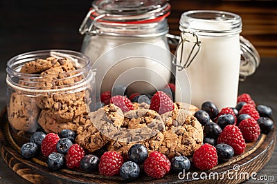 Biscuits, milk, flour recipients and forest fruits placed on rounded wooden platter close-up. Stock Photo