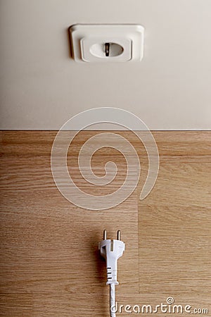 A bit more. White power socket on beige wall at low height from the floor and a short cable Stock Photo