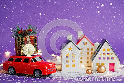 Bitcoin coin on red retro car past houses with fairy lights and snow, Christmas tree with gift boxes on roof. Violet background. Stock Photo