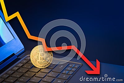 Bitcoin on laptop keyboard with arrow pointing down Stock Photo