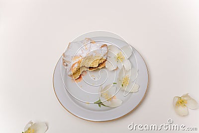 Bitten tender sand tart cake with powdered sugar on plate with some jasmine flowers around on white table. Sweet pastry Stock Photo