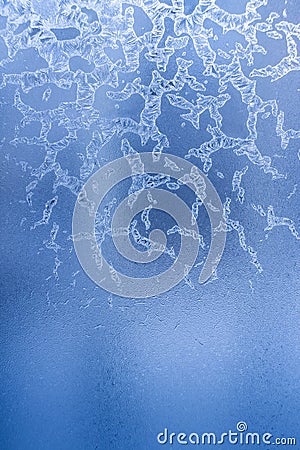 Bizarre frosty pattern of ice crystals on blue frozen winter window. Stock Photo