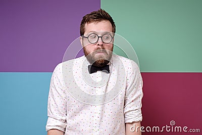 Bizarre man in round glasses, a shirt and a bow tie hunched shoulders in bewilderment and looks down with a strange Stock Photo