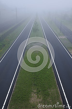 Bizarre perspective misty view by roads and train tracks with grass fields in between Stock Photo