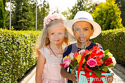 Black african american boy kid gives flowers to girl child on birthday. Little adorable children in park. Childhood and love. Stock Photo