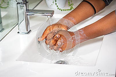 Black African Australian woman washing hands with soap in sink Stock Photo