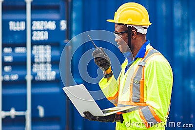 Black African happy worker working in logistic communication using radio and laptop to control loading containers at port cargo to Stock Photo