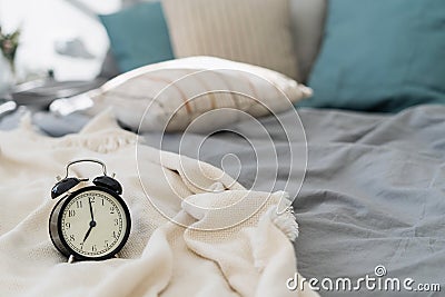 Black analog alarm clock standing on bed Stock Photo