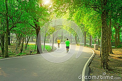 A black asfalt concrete jogging track in a public park, two people wearing yellow and green T shirt running on curve shape way Stock Photo