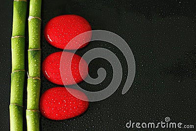 Black background with bamboo branch on the left and red zen pebbles with drops of water Stock Photo