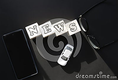 On a black background on white cubes, the inscription - news, next to black-rimmed glasses, a phone and a white toy car. Stock Photo