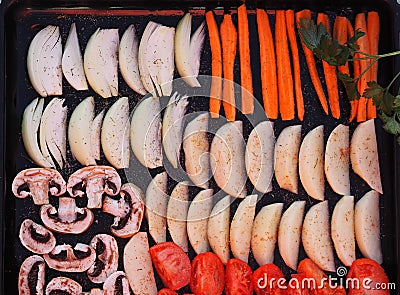 Black baking tray from a home oven with sliced vegetables for baking or drying.Homemade cooking with chips and baked vegetables. Stock Photo