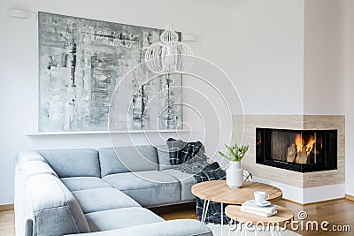 Black blanket thrown on grey corner lounge in white living room interior with fireplace, fresh tulips in vase and big modern pain Stock Photo