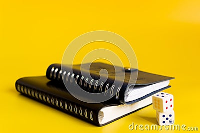 Black and blue notebooks on a yellow background with white dice Stock Photo