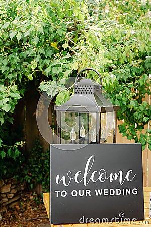 Black board wtih white welcome sign on wooden table with vintage alntern and green background Stock Photo