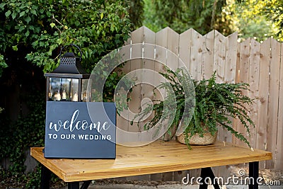 Black board wtih white welcome sign on wooden table with vintage alntern and green background Stock Photo