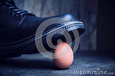 Black boot steps on a fragile chicken egg. Concept, weak defenseless, care and custody Stock Photo