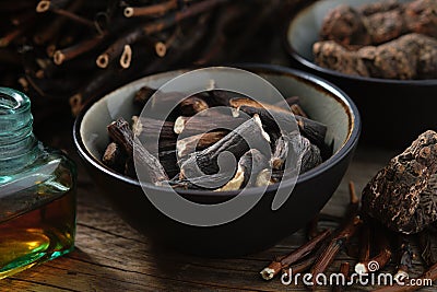 Bowl of Common comfrey or symphytum officinale roots. Bottle of infusion or tincture. Dried comfrey officinalis roots, Bistoret. Stock Photo