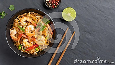In a black bowl, noodles, veggies, and prawns are stir-fried. slate background. higher perspective Stock Photo