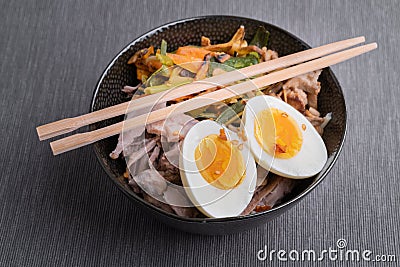 Black bowl of ramen noodles with boiled eggs, veggies and turkey meet, ready to be poured with boiling broth. Wooden Stock Photo