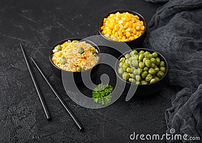 Black bowls with boiled organic basmati vegetable rice, yellow corn and peas with black chopsticks on black stone background with Stock Photo
