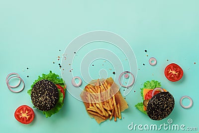 Black burger, french fries potatoes, tomatoes, cheese, onion, cucumber and lettuce on blue background. Top view. Fast food banner Stock Photo